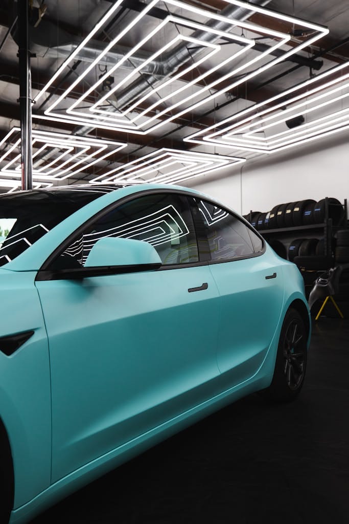 Sleek matte blue car captured inside a modern auto detailing studio with geometric ceiling lights.