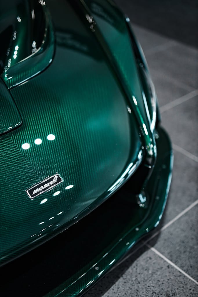 Dark green supercar hood with carbon fiber texture in a showroom setting.